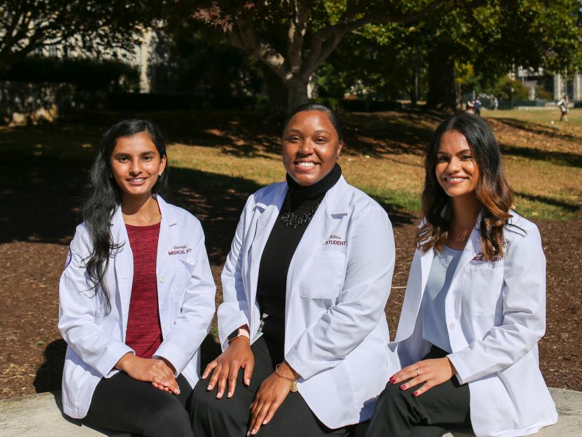 three medical students wear their white coats following the ceremony