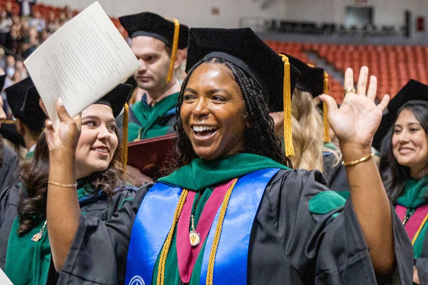 VCOM-Louisiana student in regalia arms raised smiling