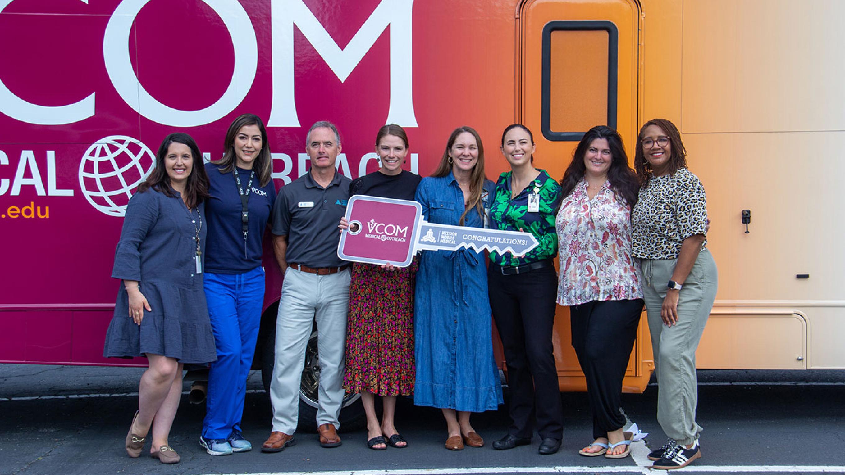 VCOM-Carolinas faculty standing in front of a mobile medical unit holding an oversized key