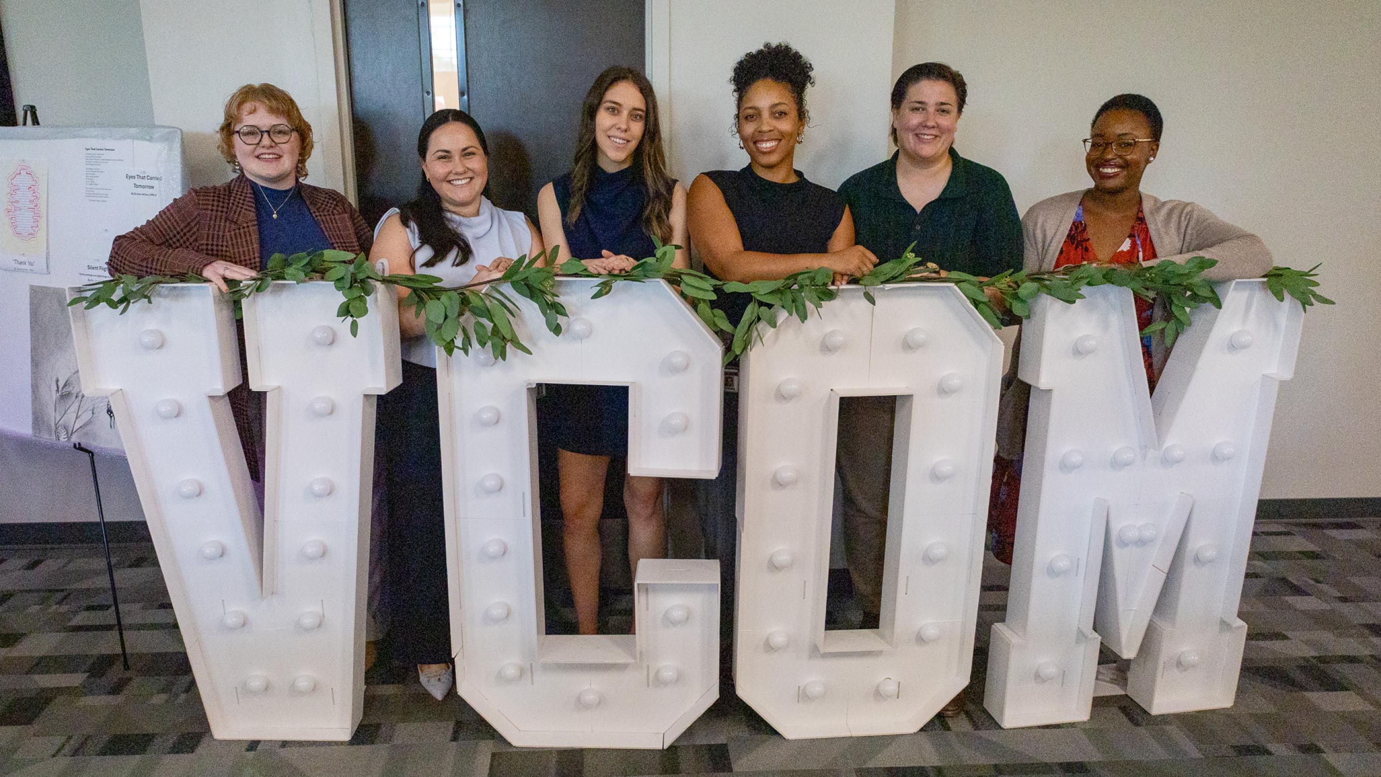 VCOM-Louisiana students gathered around a giant VCOM light up sign
