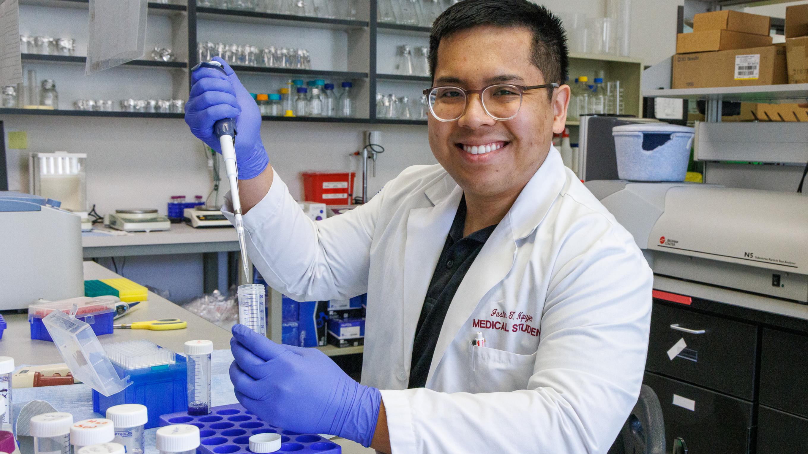 Justin Nguyen smiling in a lab wearing gloves doing research