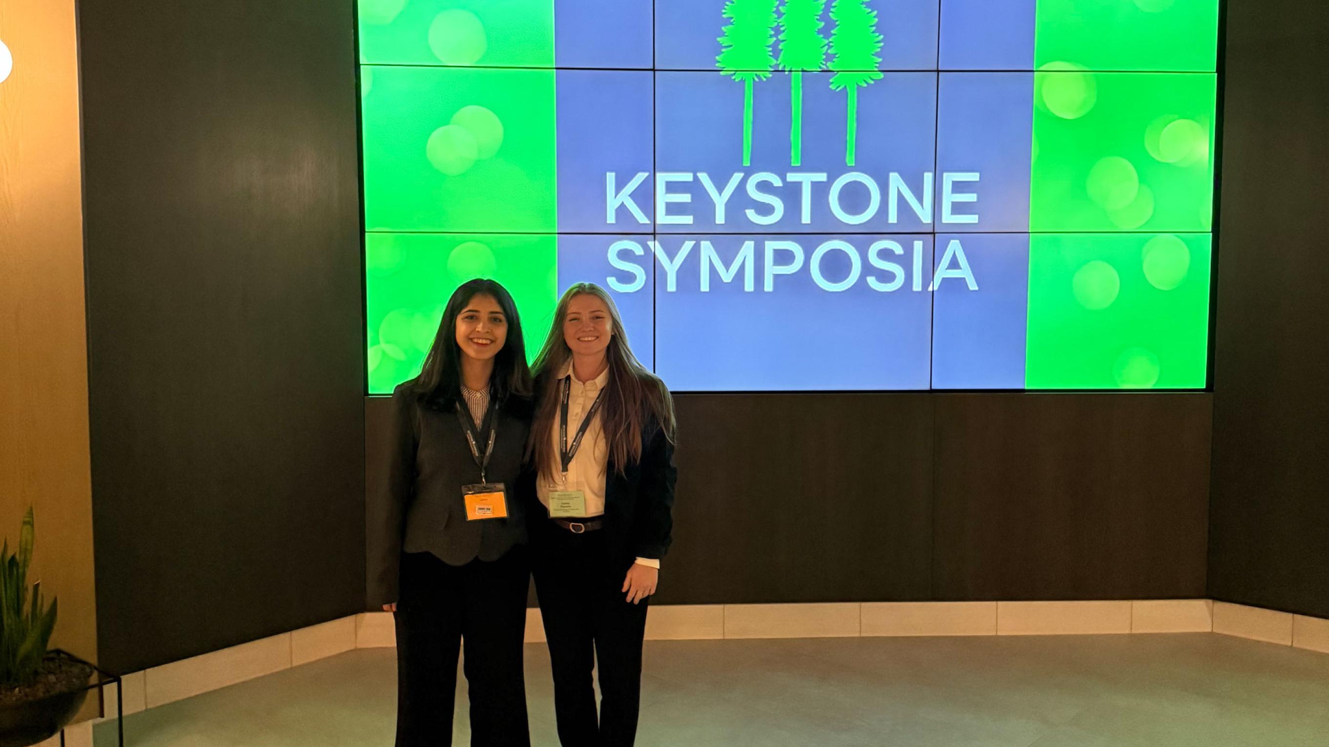Camila Pacocha and Shadika Panta standing in front of a Keystone Symposia banner graphic