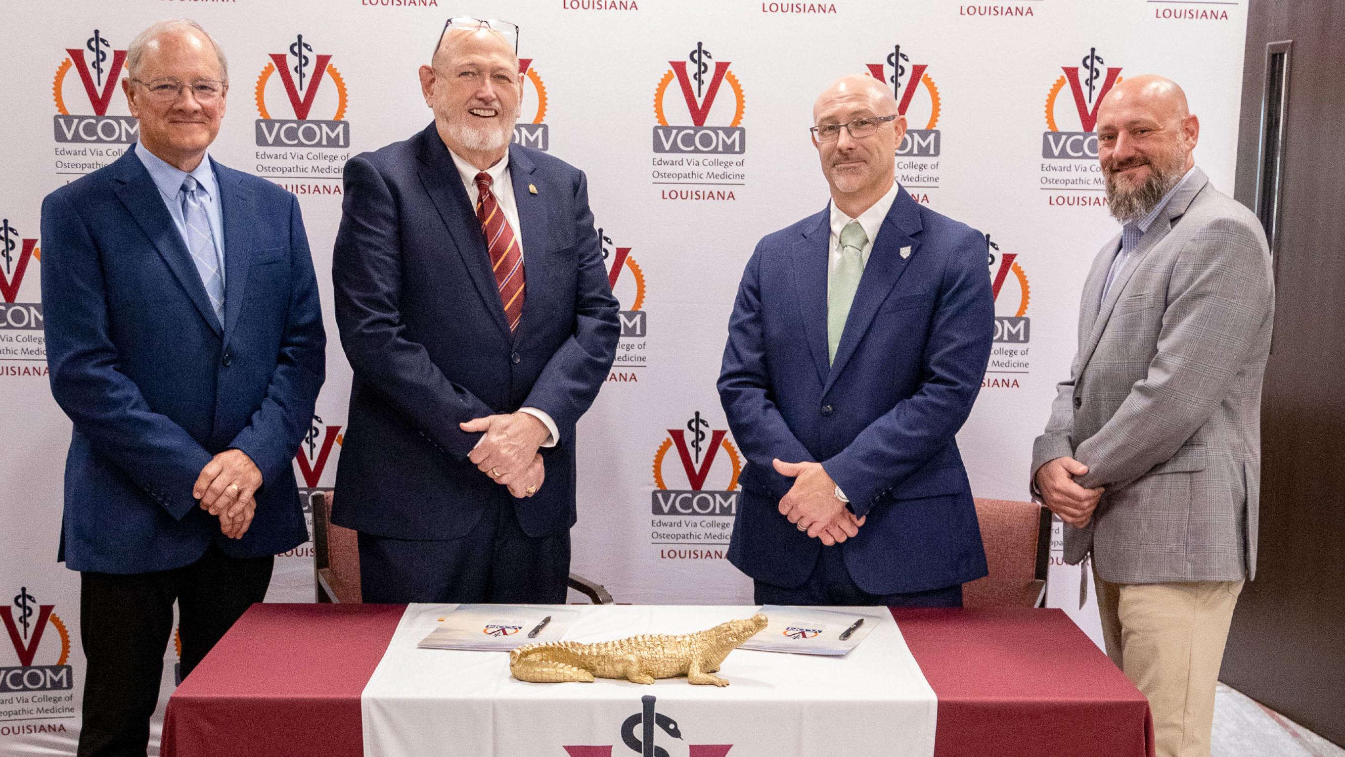 Representatives from VCOM and FranU standing in front of a signing table smiling