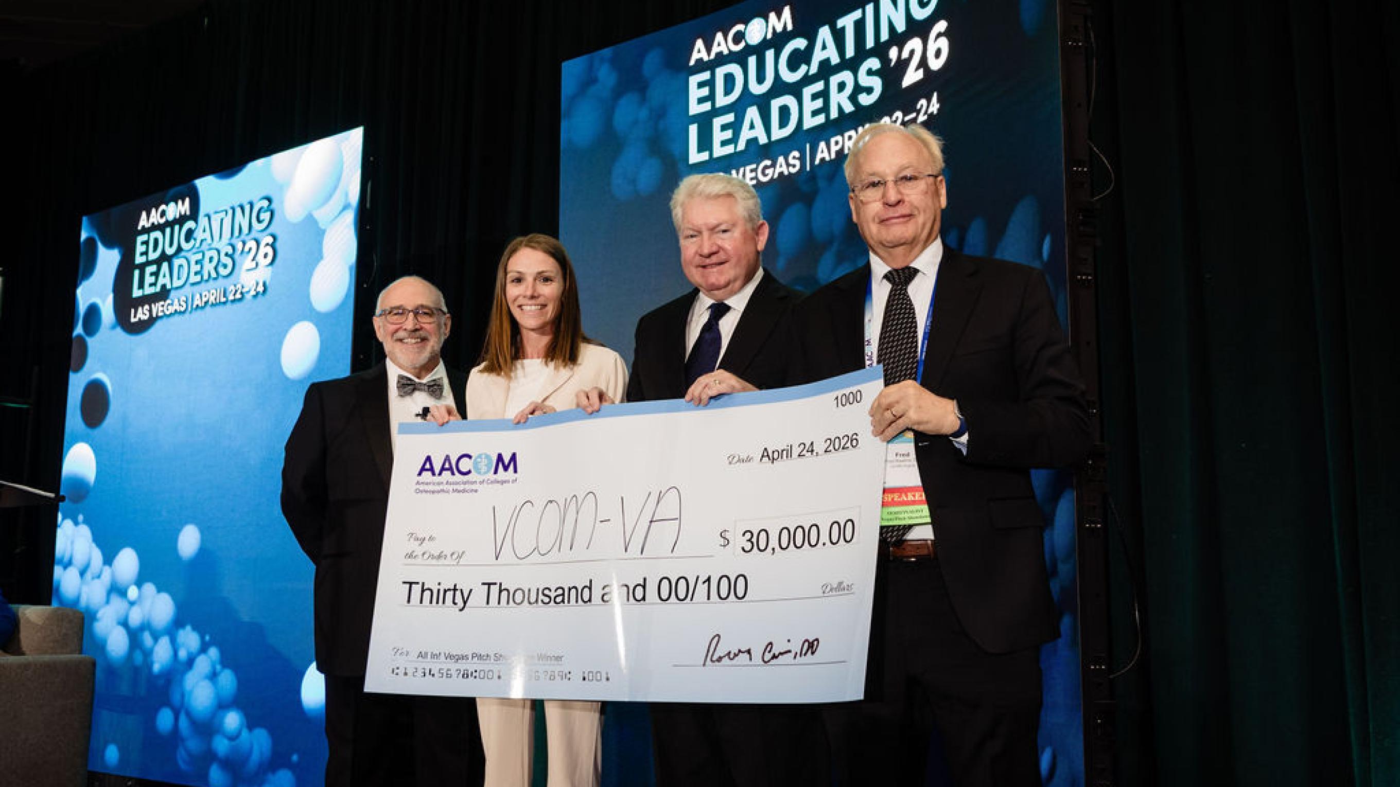 Representatives from VCOM standing on a stage holding a large check