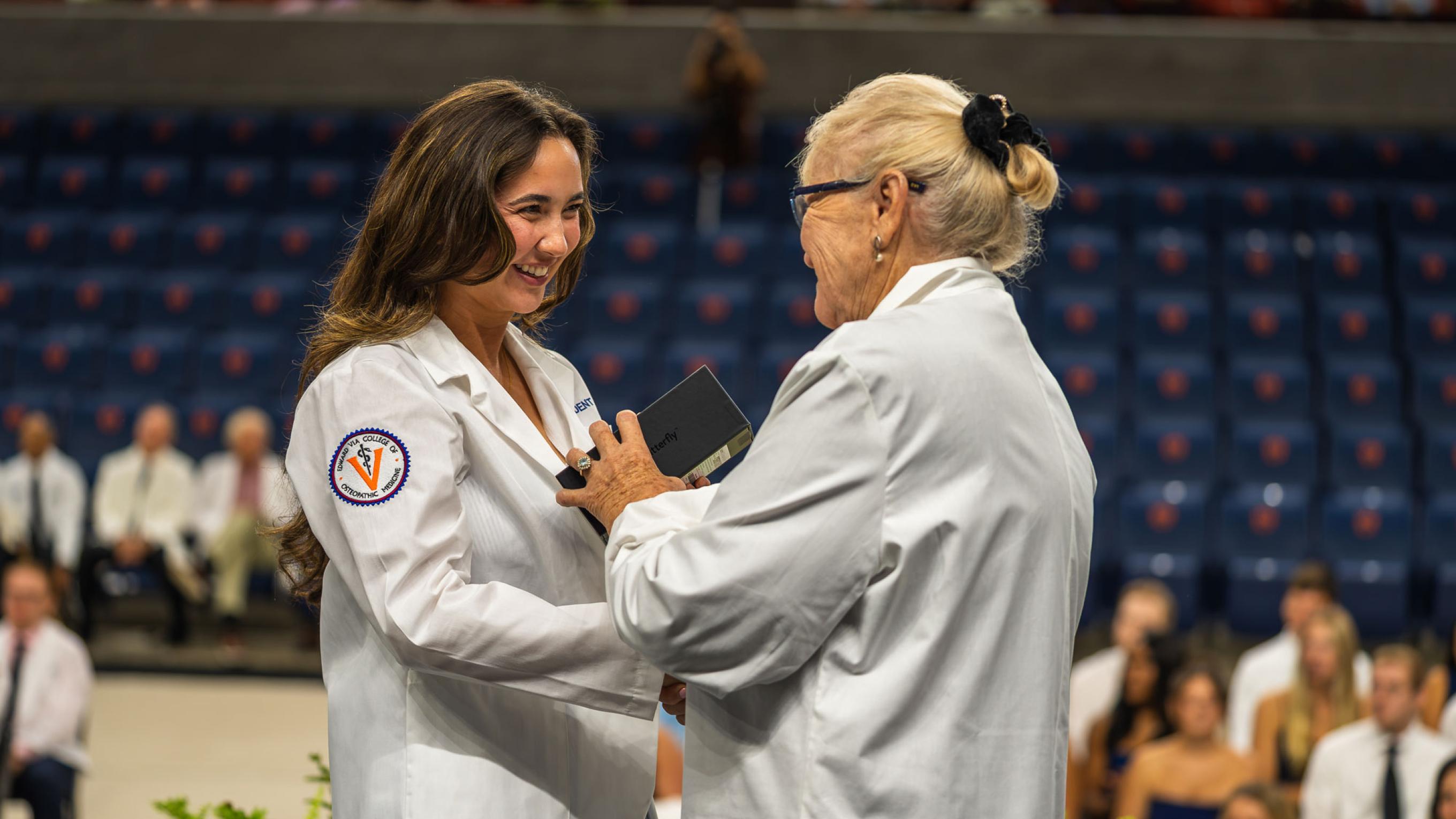 Dr Tooke-Rawlins handing a Butterfly Network portable ultrasound device to a medical student in a white coat on a stage