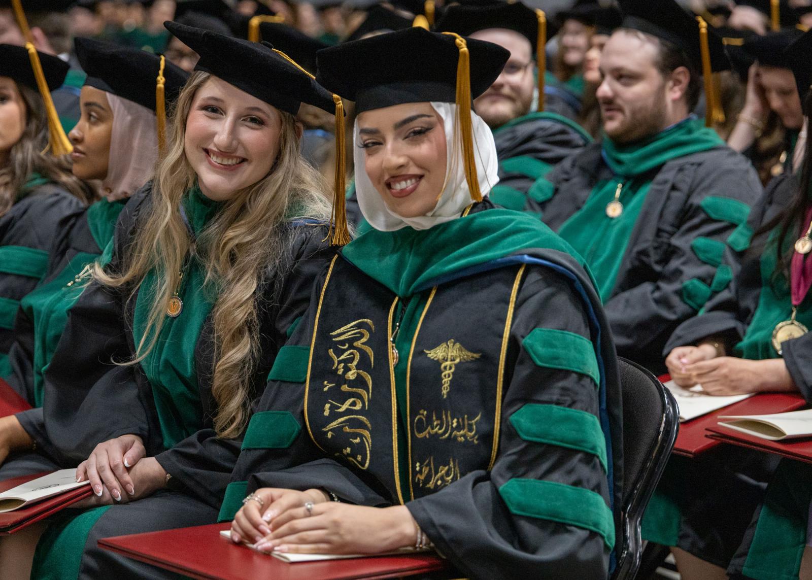 Two seated VCOM class of 2025 graduates smiling at the camera during the graduation ceremony