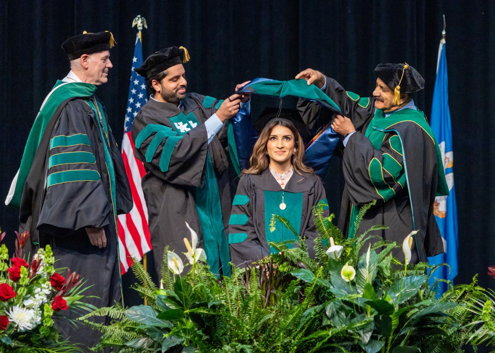VCOM class of 2025 graduate on stage being hooded by family members