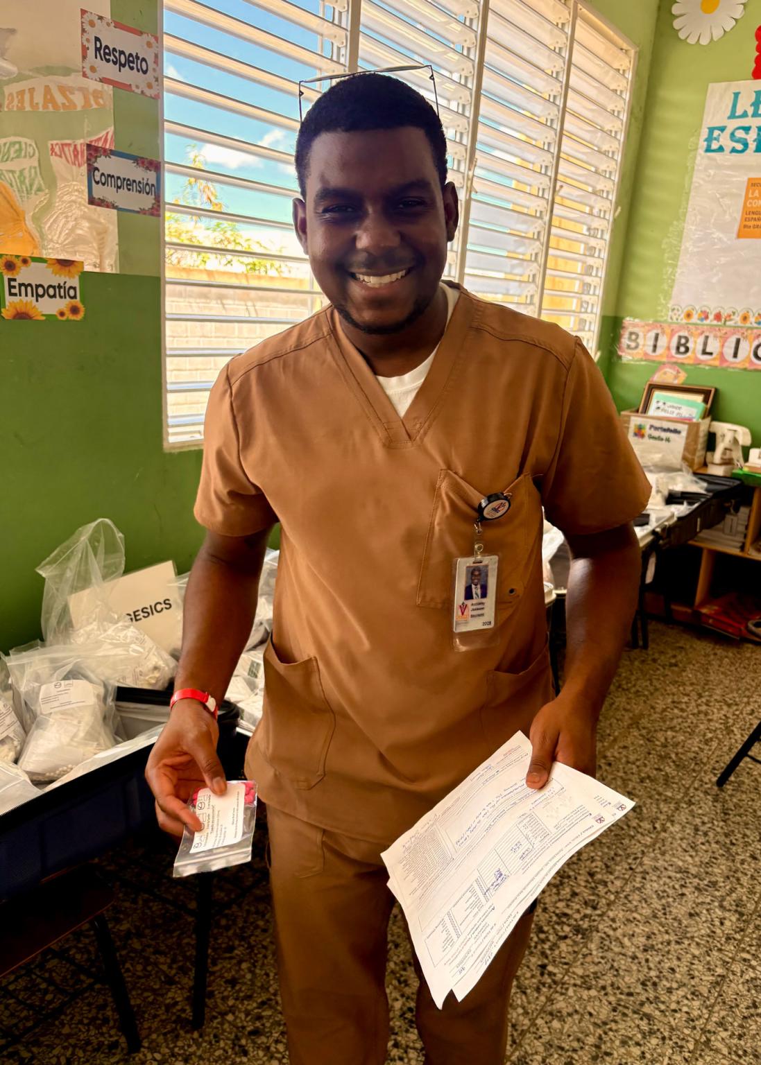 VCOM medical student in scrubs holding paperwork and smiling