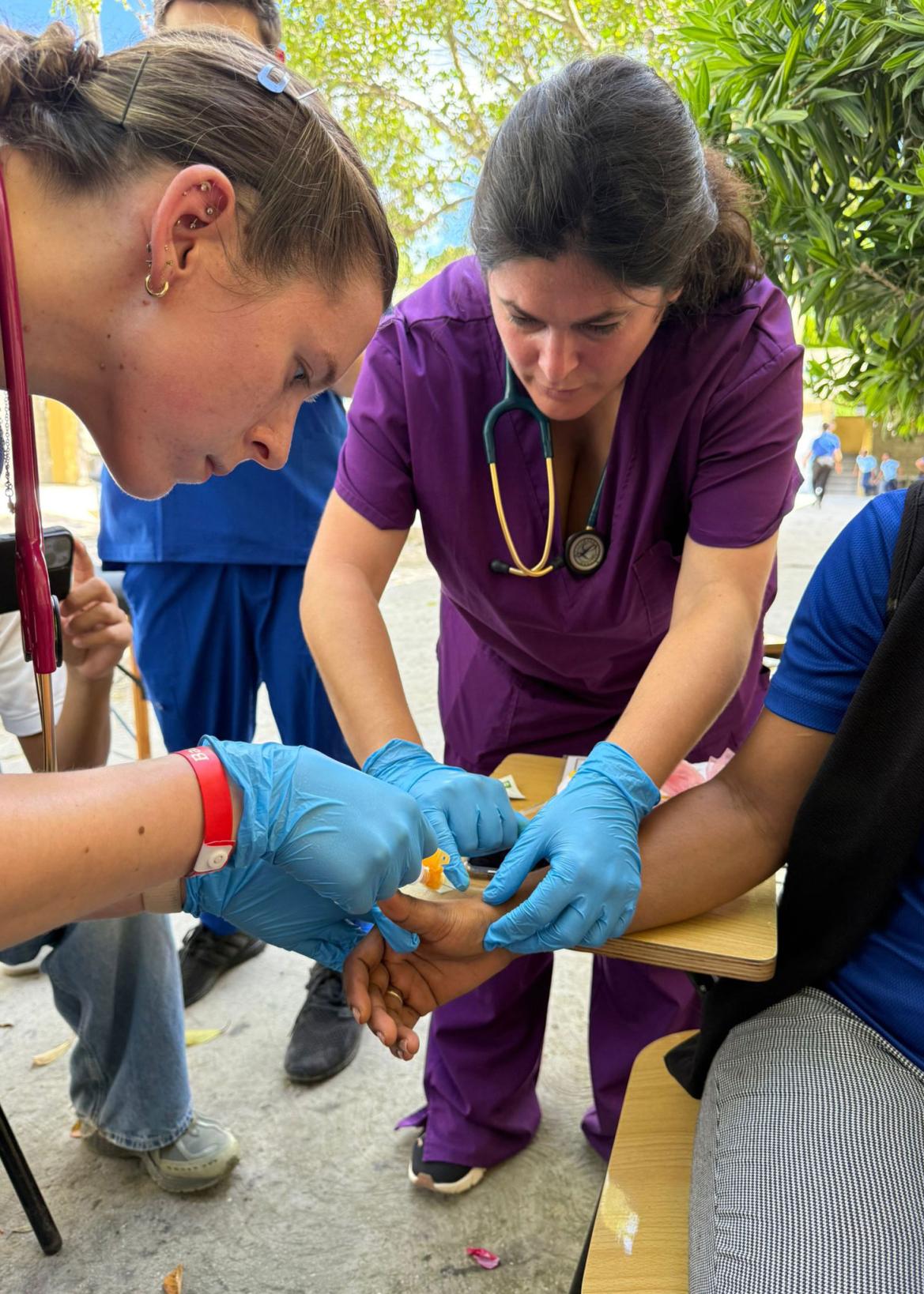 Two medical students wearing gloves holding a patient's arm