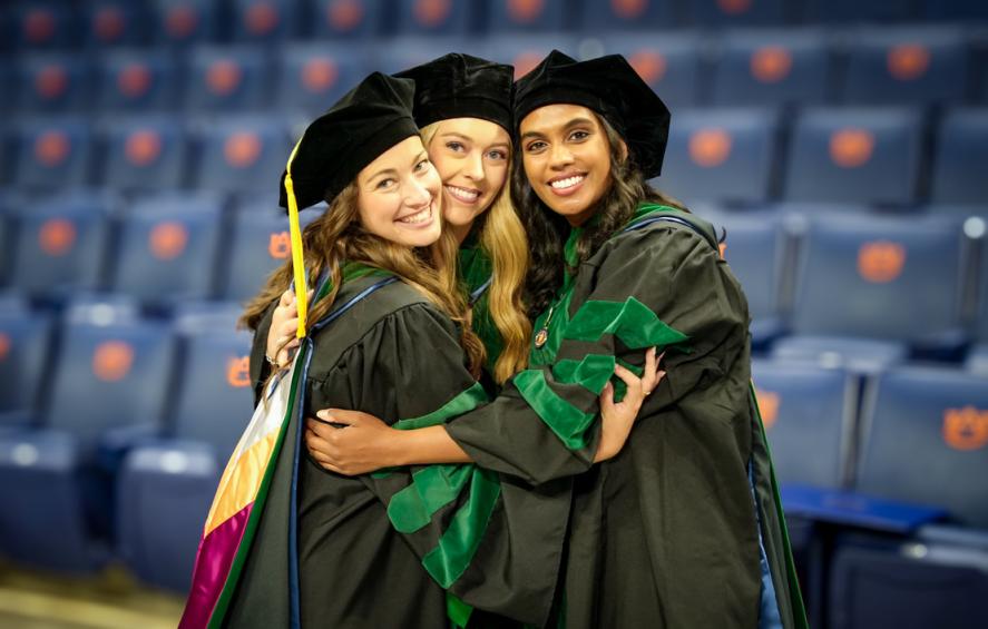 Three VCOM-Auburn class of 2026 graduates in regalia hugging and smiling