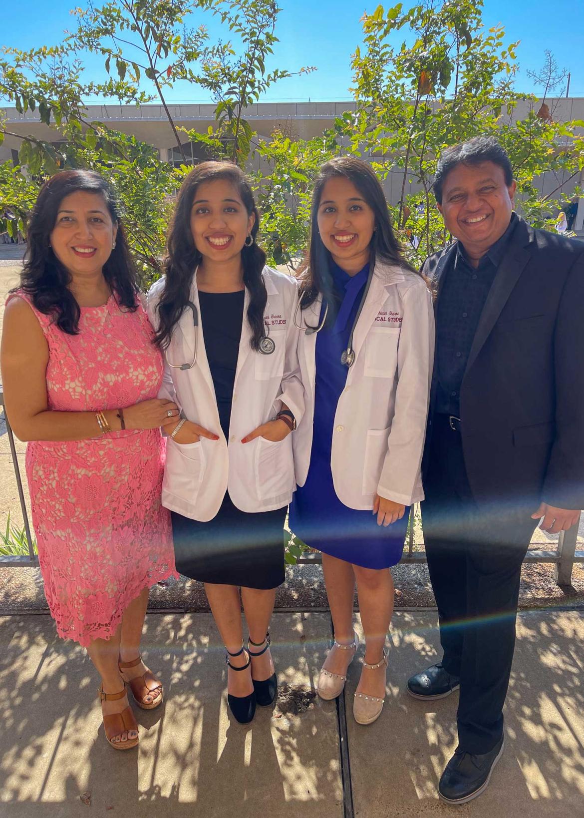 Drs. Ishani and Shivani Sharma in whitecoats standing with their parents