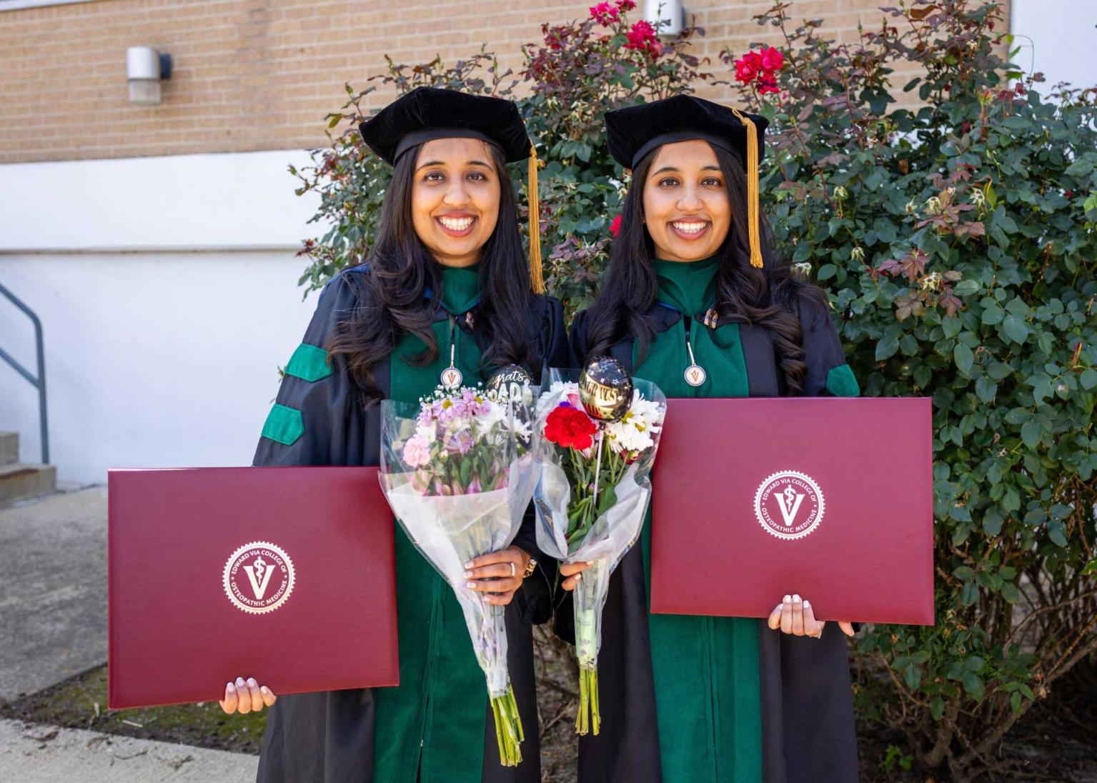 Drs. Ishani and Shivani Sharma in regalia holding their diplomas