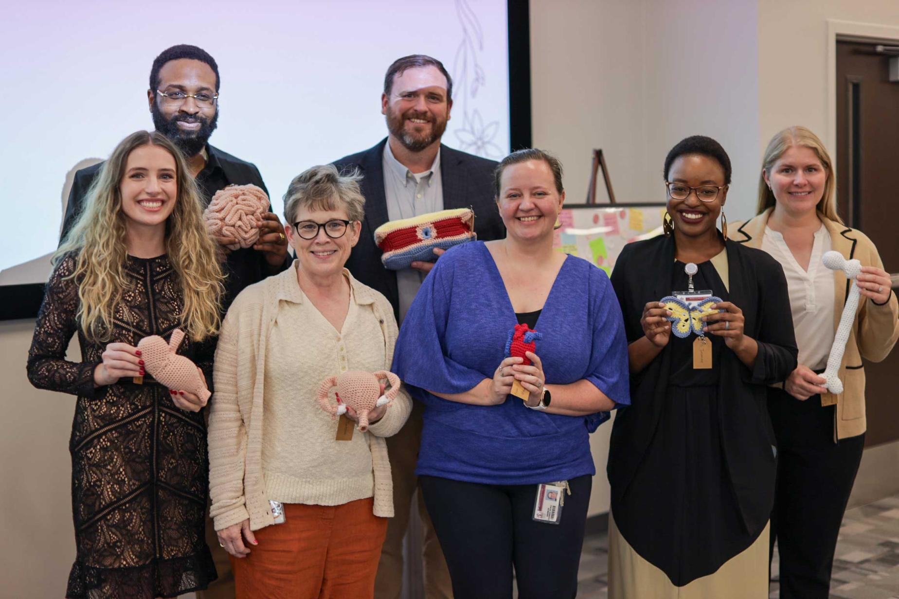 Students and staff holding hand-knitted human anatomical crafts.