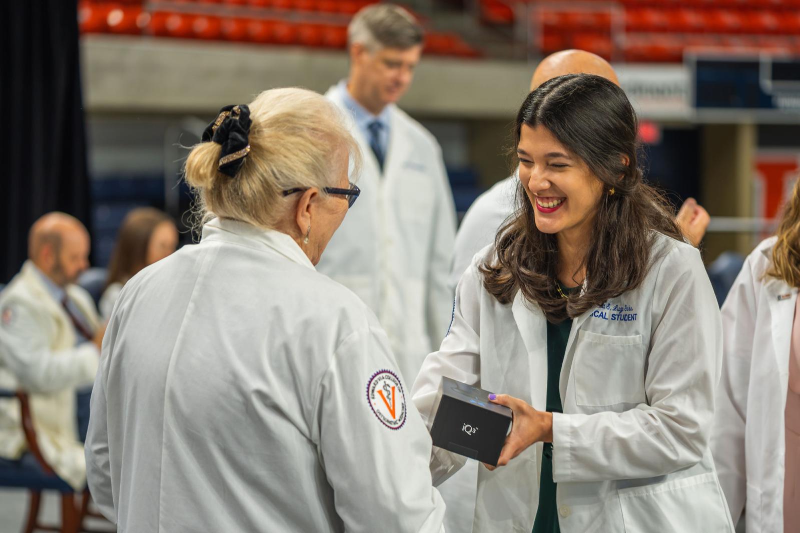 VCOM president Dr Tooke-Rawlins handing a Butterfly Network portable ultrasound device to a medical student.