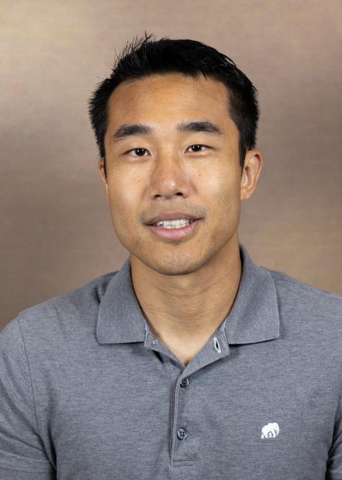 A man smiling wearing a gray polo shirt
