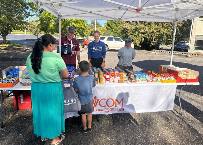 VCOM Outreach table with free food. Mother and child picking up food