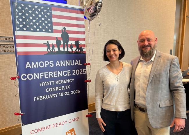 Sydney Gould standing in front of AMOPS Conference poster