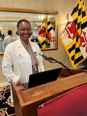 Ariana Martin in her whitecoat smiling at a speaker's podium