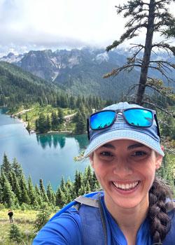 Sydney Gould selfie on a hike with mountains and a lake in the background