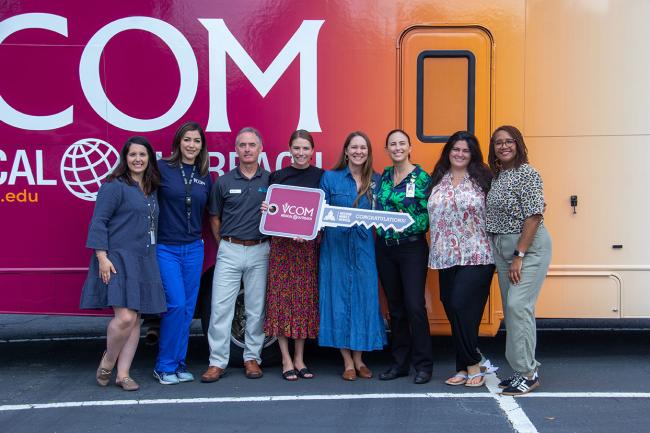 VCOM-Carolinas faculty standing in front of a mobile medical unit holding an oversized key