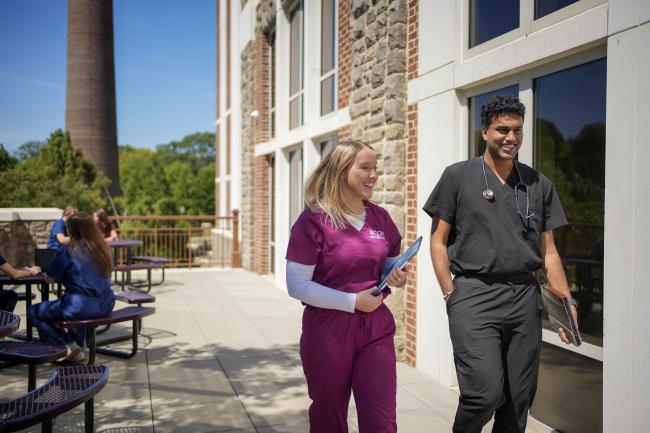 Two VCOM-Carolinas students in scrubs walking and smiling.
