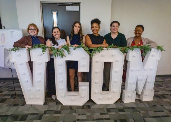 VCOM-Louisiana students gathered around a giant VCOM light up sign