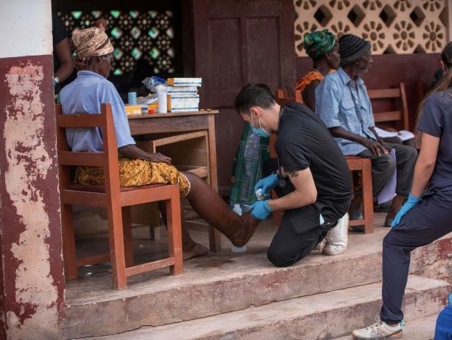 Robert Eysler kneeling next to a patient's leg during a mission trip