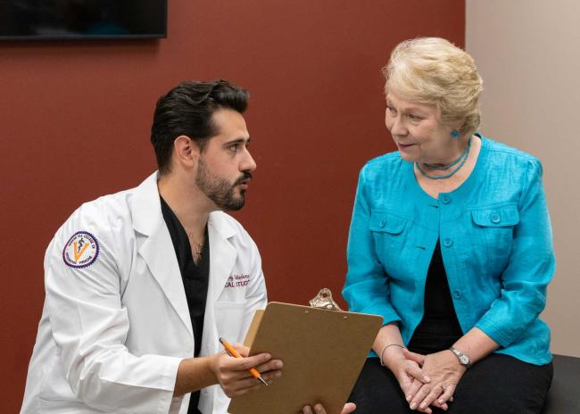 VCOM-Louisiana student with a clipboard talking to a standardized patient