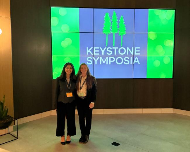 Camila Pacocha and Shadika Panta standing in front of a Keystone Symposia banner graphic