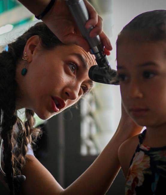 VCOM student in Honduras holding otoscope to a child's ear