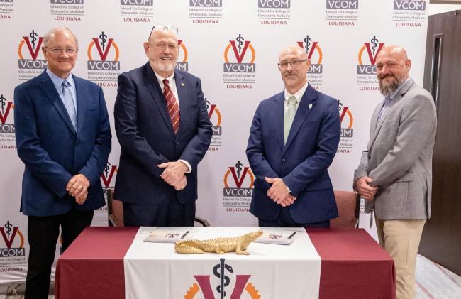 Representatives from VCOM and FranU standing in front of a signing table smiling