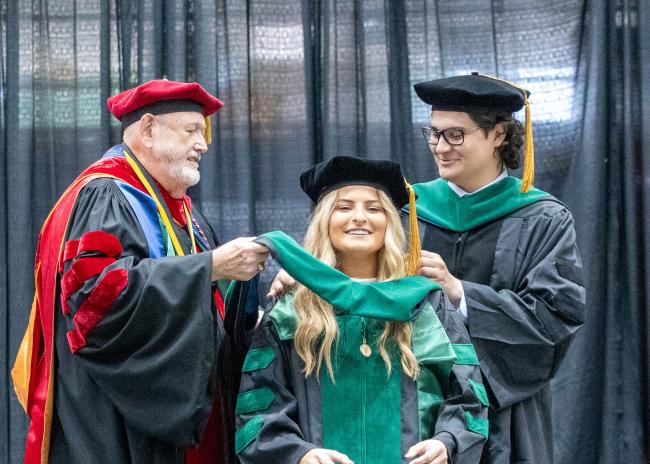 VCOM Louisiana class of 2026 graduate being hooded on stage by two other doctors
