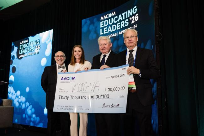 Representatives from VCOM standing on a stage holding a large check
