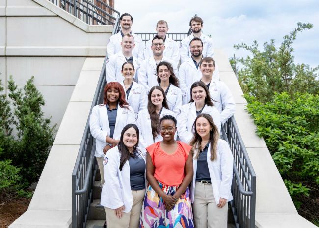 Jasmine Belton and VCOM-Louisiana students in white coats standing outside on a staircase smiling.