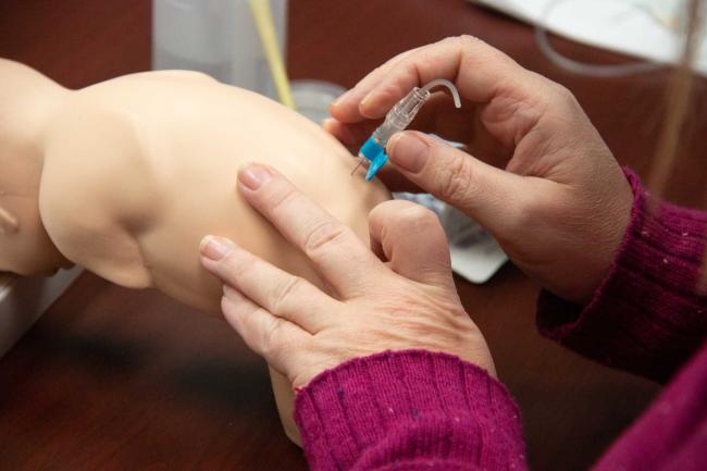 Medical student inserting a needle into a pediatric manikin
