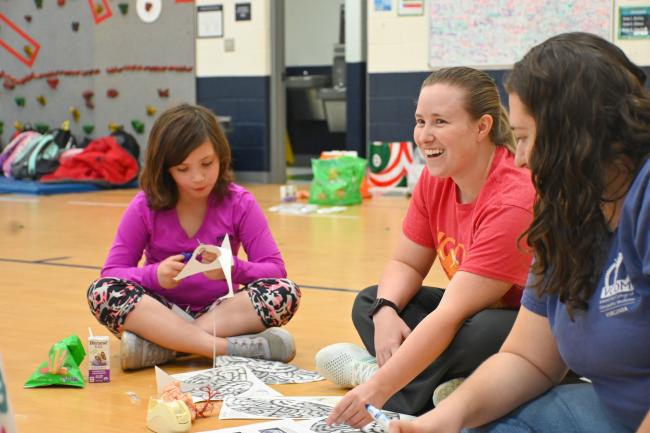 Medical student sitting on the floor with child working on a paper brain project