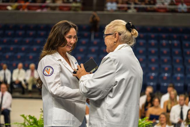 Dr Tooke-Rawlins handing a Butterfly Network portable ultrasound device to a medical student in a white coat on a stage