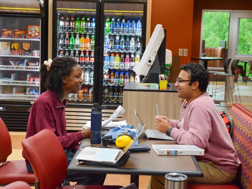 Two students surrounded by study materials talking at a cafe table.