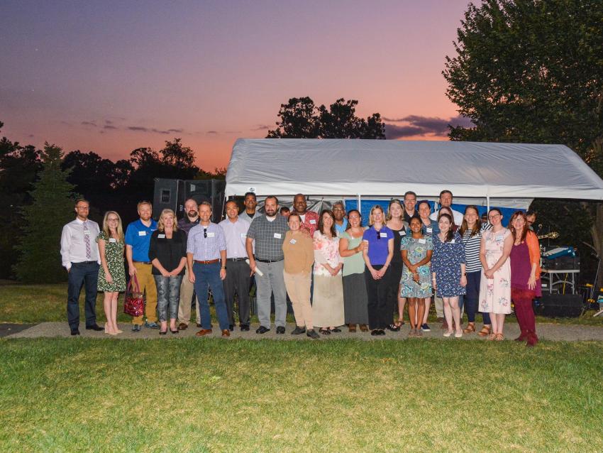 A large group of people posing in front of a tent at an outdoor event.