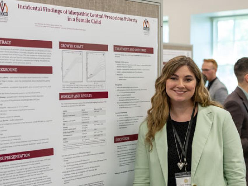 Student smiling next to research poster