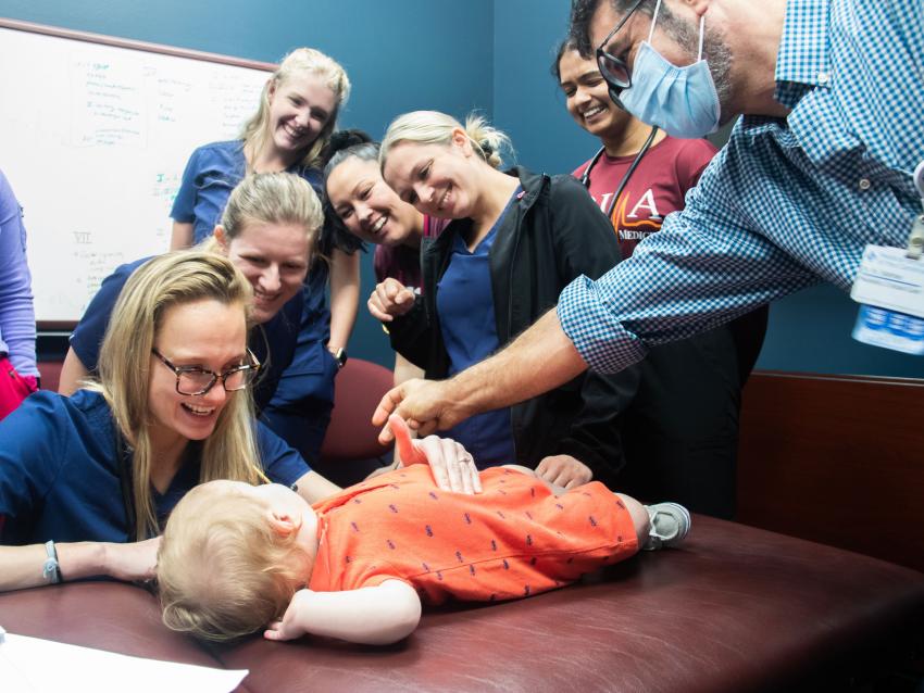 Carolinas medical students gathered around a happy baby on an exam table