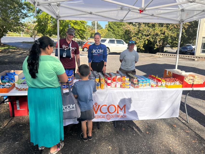 VCOM Outreach table with free food. Mother and child picking up food