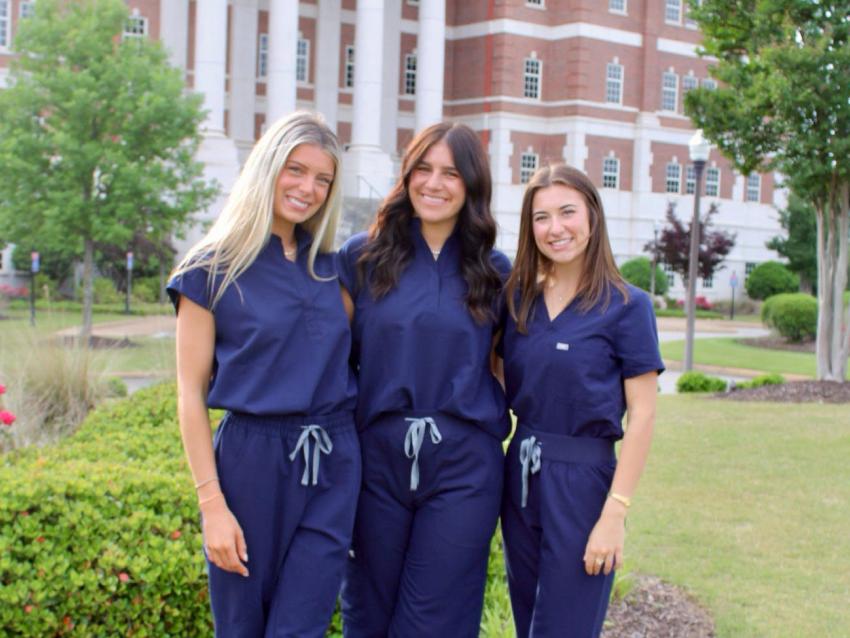 Three MHSA students in scrubs smiling outside VCOM-Auburn