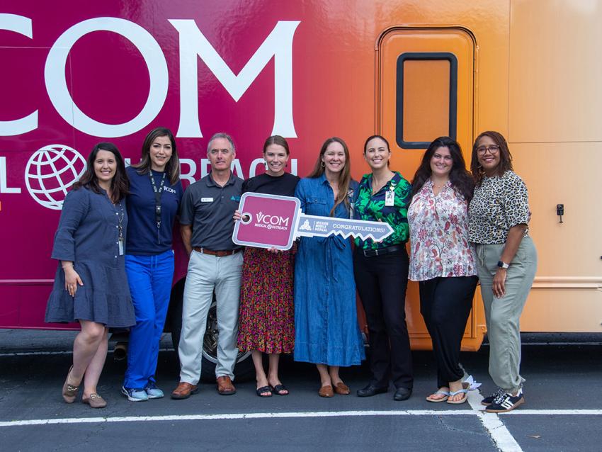 VCOM-Carolinas faculty standing in front of a mobile medical unit holding an oversized key