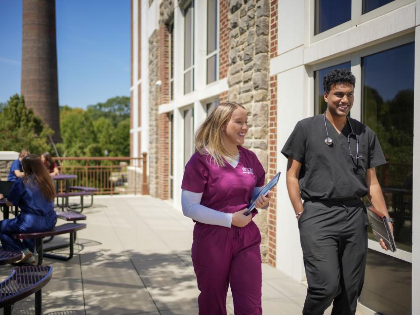 Two VCOM-Carolinas students in scrubs walking and smiling.