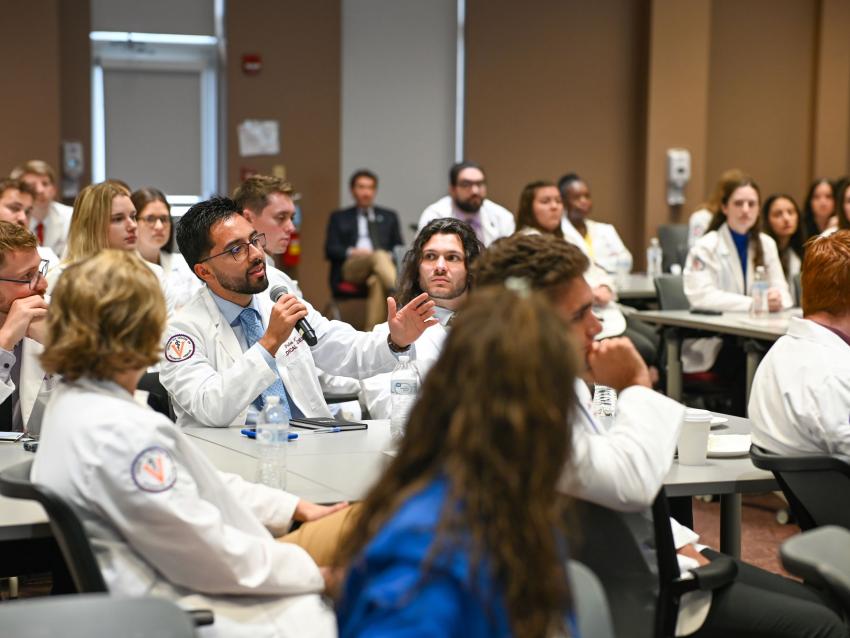 VCOM-Virginia CORE Symposium students in white coats with one person holding a microphone speaking 