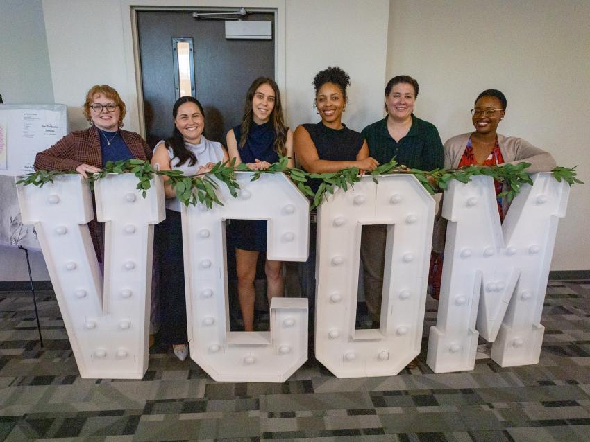 VCOM-Louisiana students gathered around a giant VCOM light up sign