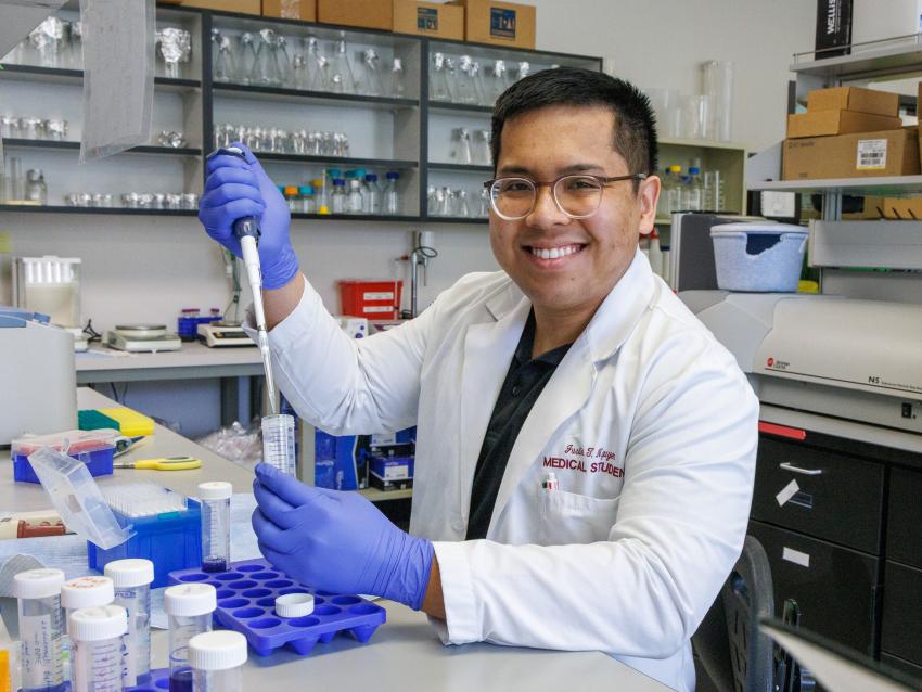 Justin Nguyen smiling in a lab wearing gloves doing research
