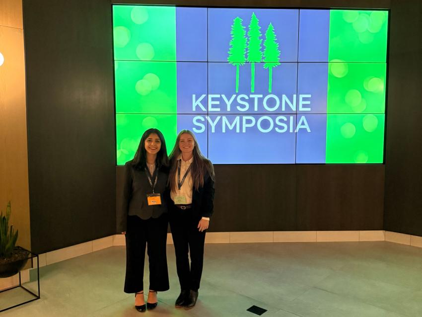 Camila Pacocha and Shadika Panta standing in front of a Keystone Symposia banner graphic