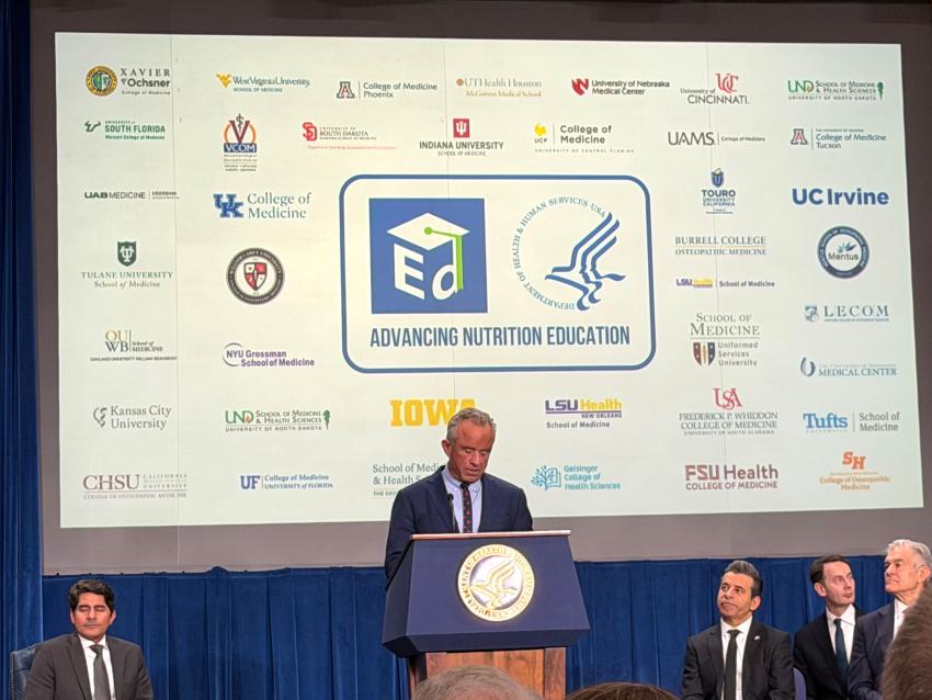 RFK Jr speaking in front of a screen of medical school logos